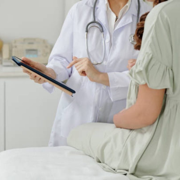 Close-up of female doctor in white coat presenting information from digital tablet to pregnant woman